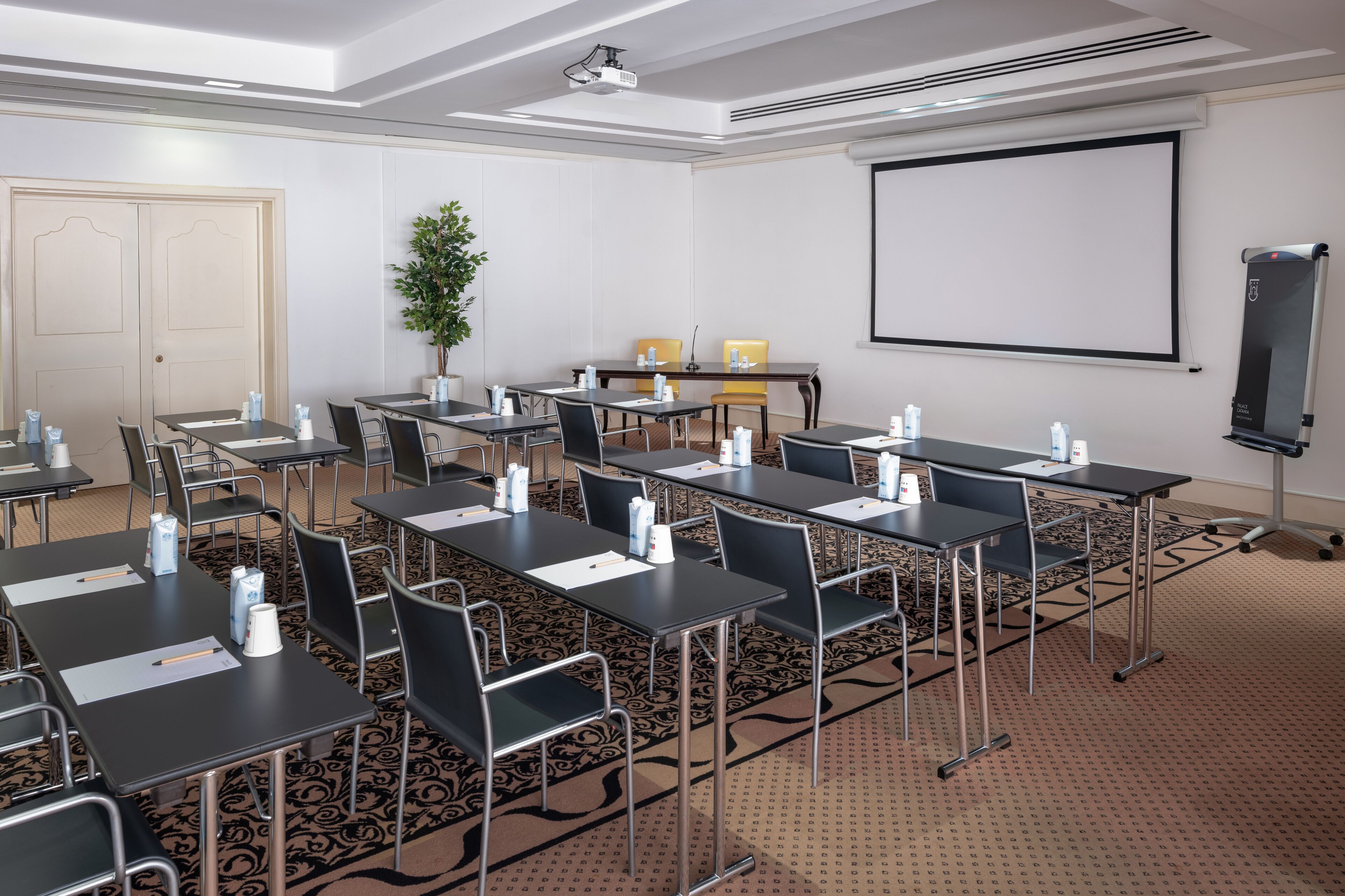 A conference room with tables, chairs, a projector screen, and a whiteboard.