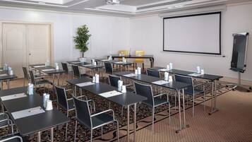 A conference room with tables, chairs, a projector screen, and a whiteboard.