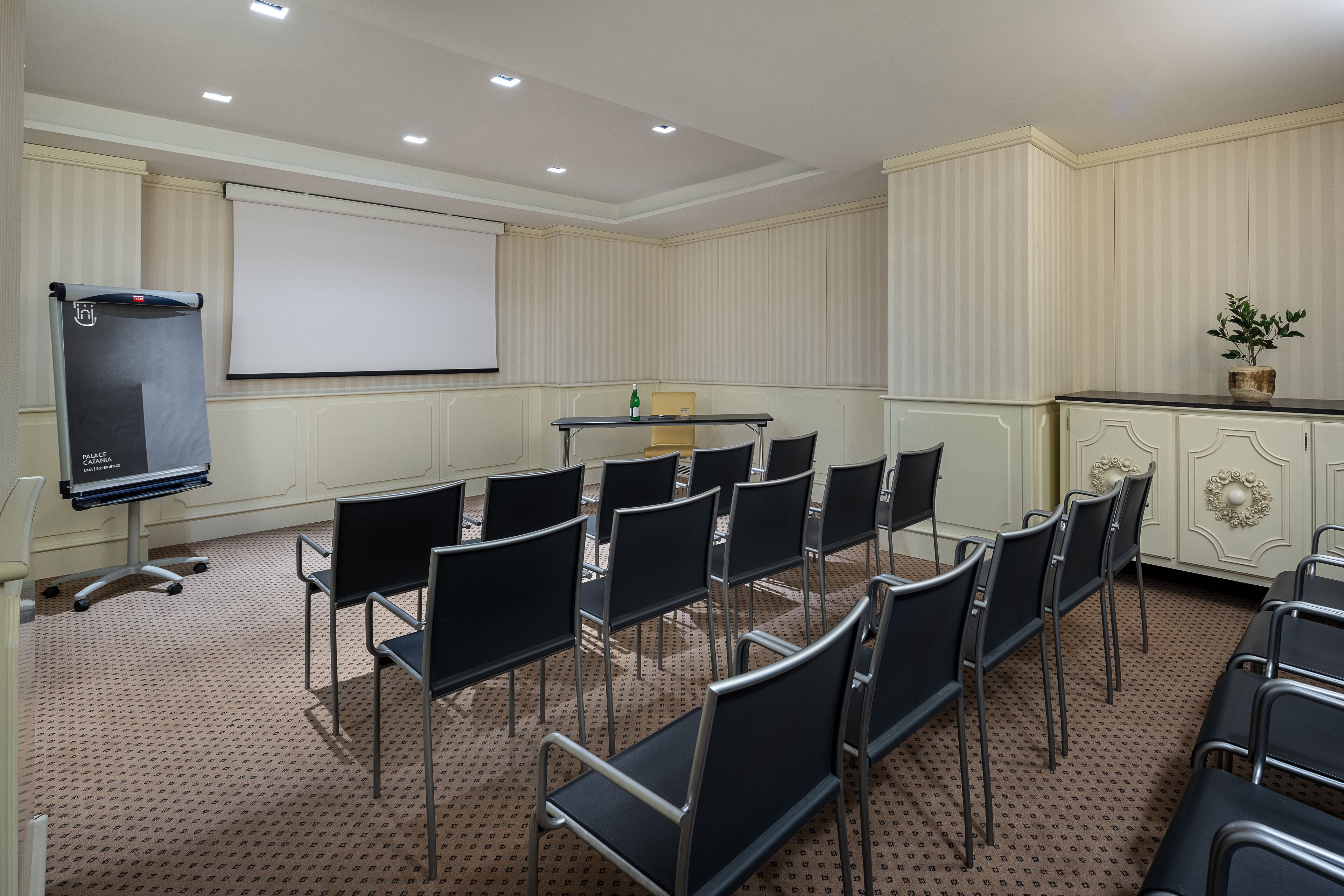 Una sala de conferencias con una pantalla de proyector, una mesa y varias sillas dispuestas para una reunión.