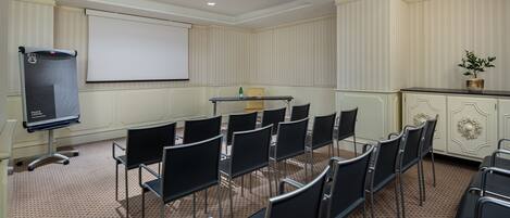 Una sala de conferencias con una pantalla de proyector, una mesa y varias sillas dispuestas para una reunión.