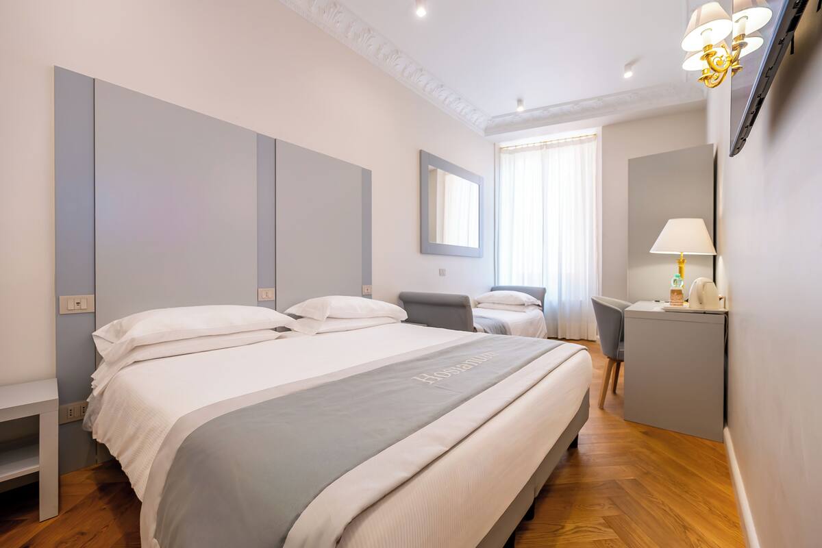 A hotel room with a large bed, a desk, a chair, and a mirror.