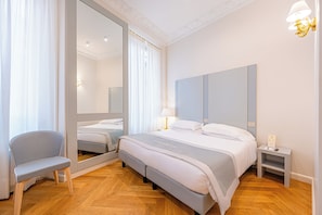 A modern bedroom with a bed, a chair, a nightstand, a mirror, and a wall-mounted light fixture. - Hosianum Palace (Rome)