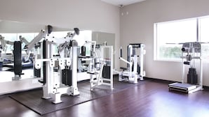 A gym with various exercise machines, a large mirror, and a window providing natural light. - Residence & Conference Centre - Oakville (Oakville)