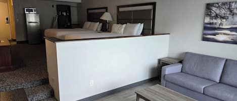 A compact hotel room with a kitchenette, a sofa, a coffee table, and a painting on the wall.