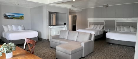 A hotel room with two beds, a sofa, a dining table, and a mirror.