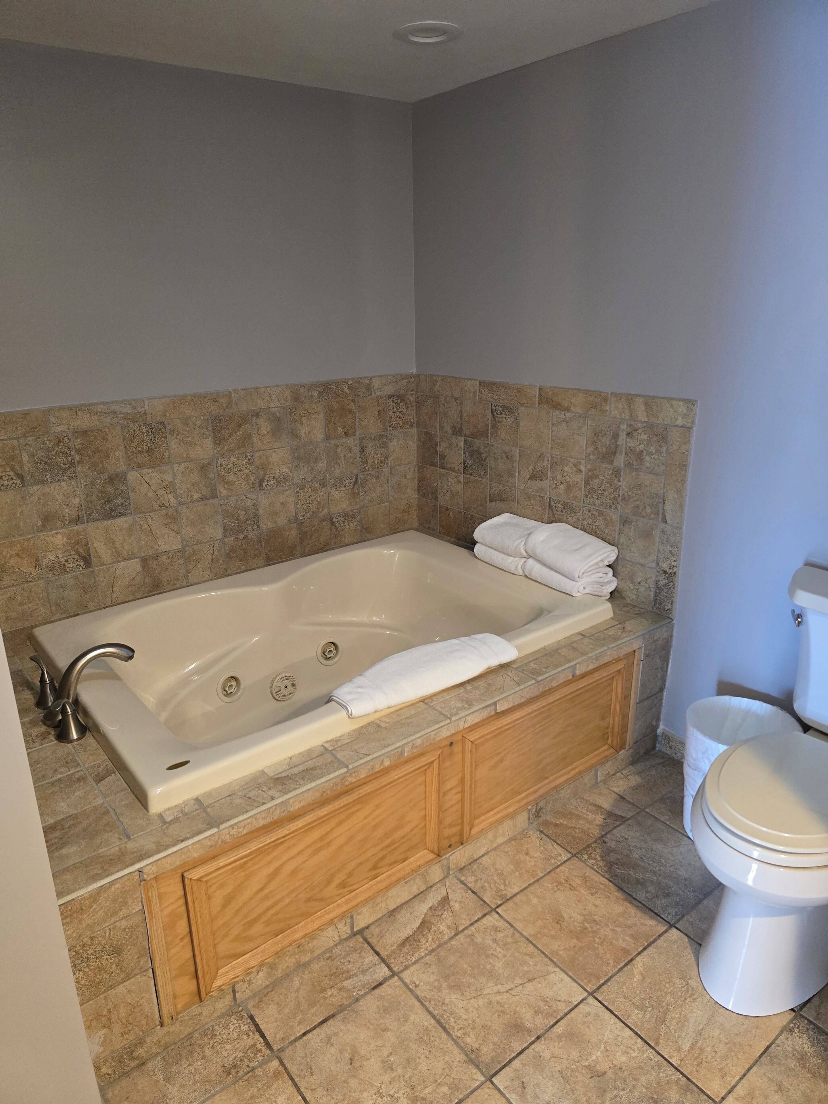 A bathroom with a large bathtub, wooden vanity, and a toilet.