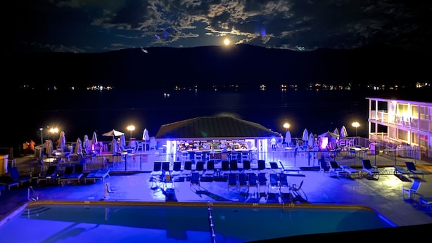 A poolside area with lounge chairs and umbrellas, a bar, and a view of the sea and mountains at night. - The Georgian Lakeside Resort (Lake George)