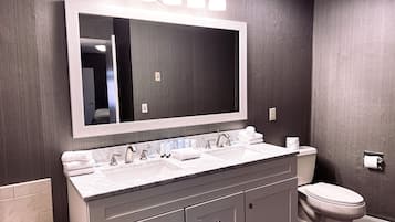 A modern bathroom with a large mirror, dual sinks, and a toilet.