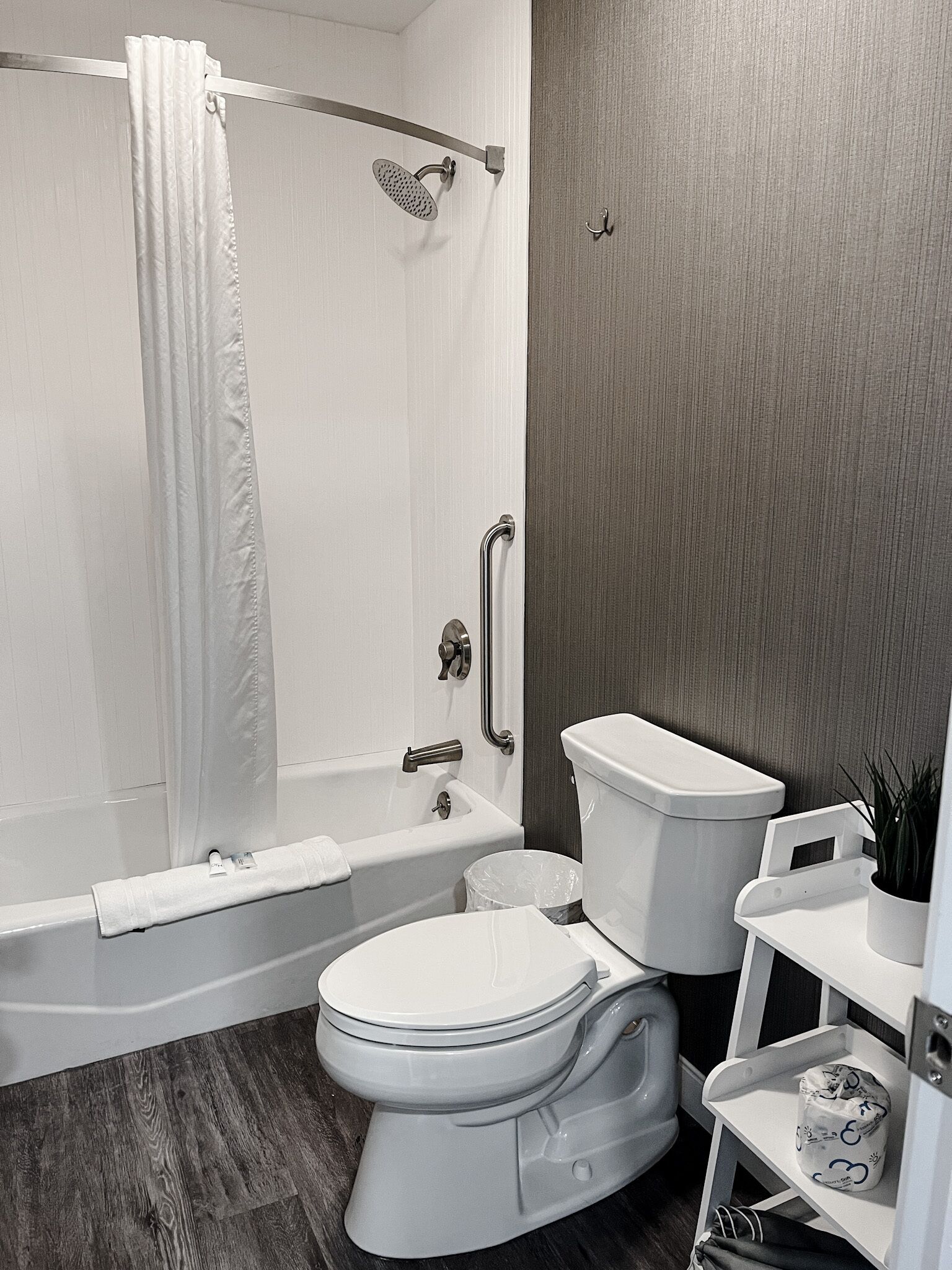 Un baño moderno con ducha, inodoro y un estante pequeño con artículos de aseo.
