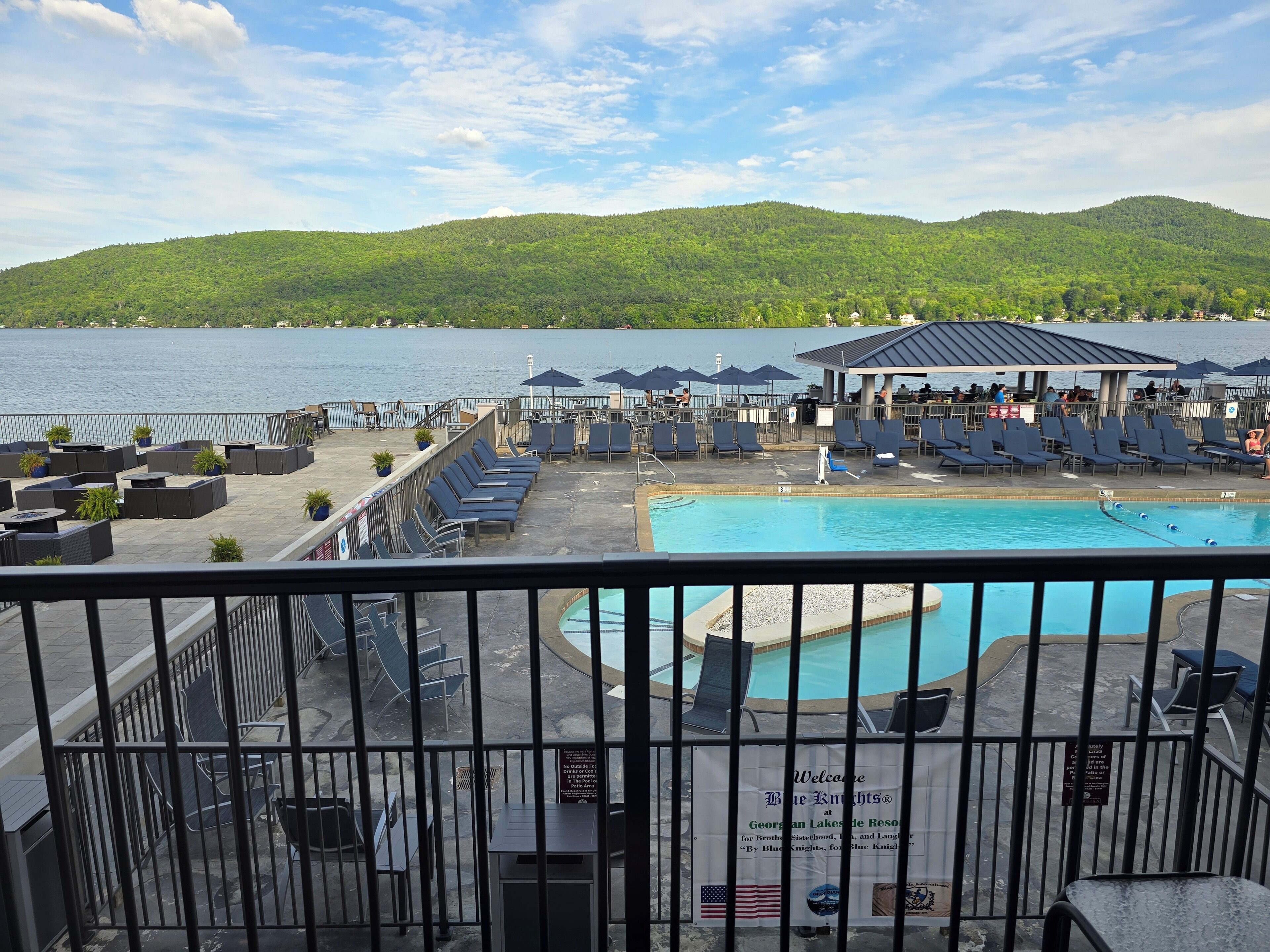 A poolside area with lounge chairs and umbrellas, overlooking a lake and hills.