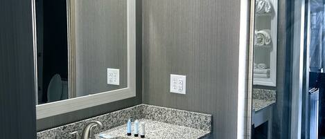 A modern bathroom with a granite countertop, a double sink, and a large mirror.