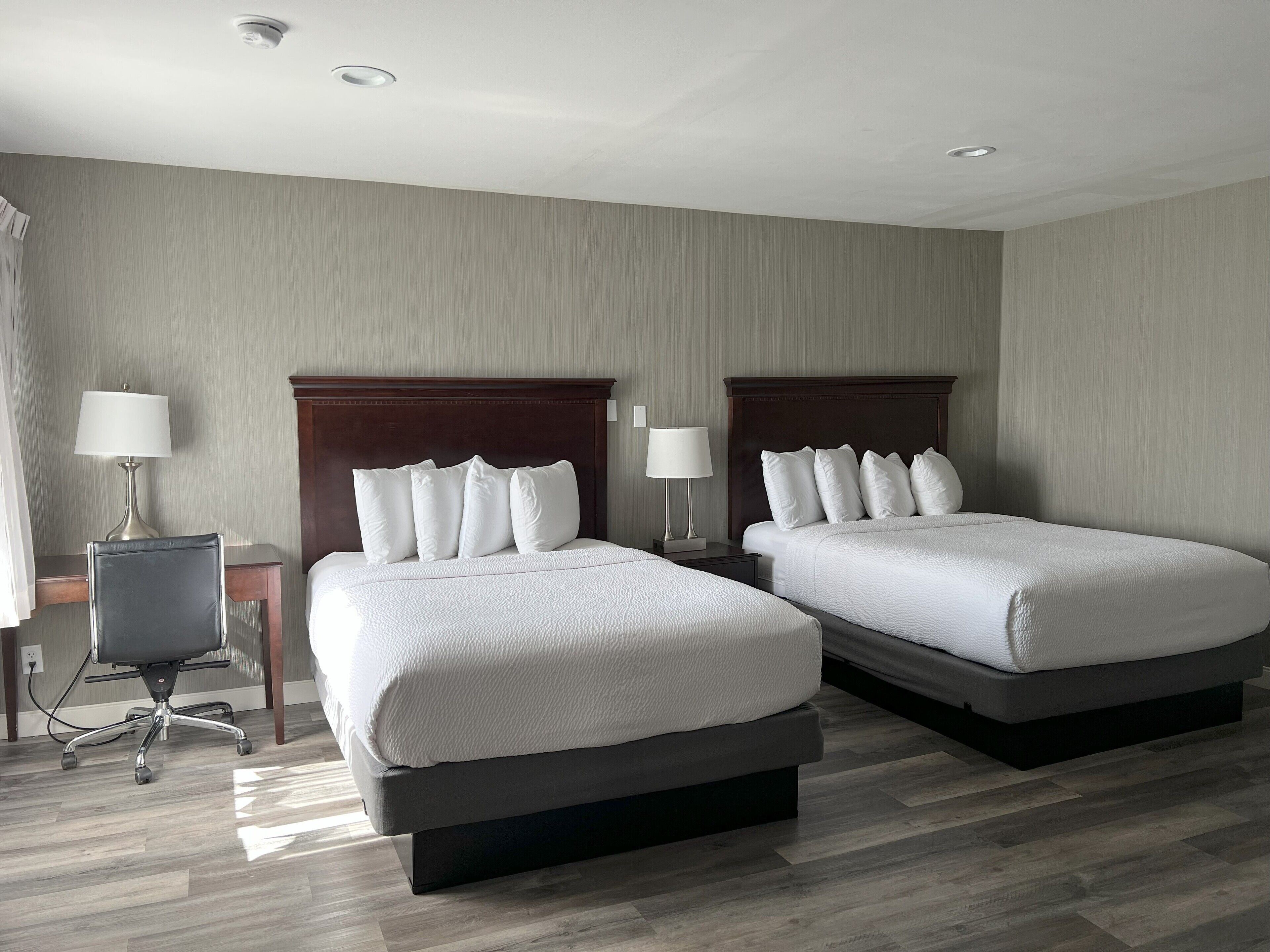 A hotel room with two beds, a desk, and a chair.
