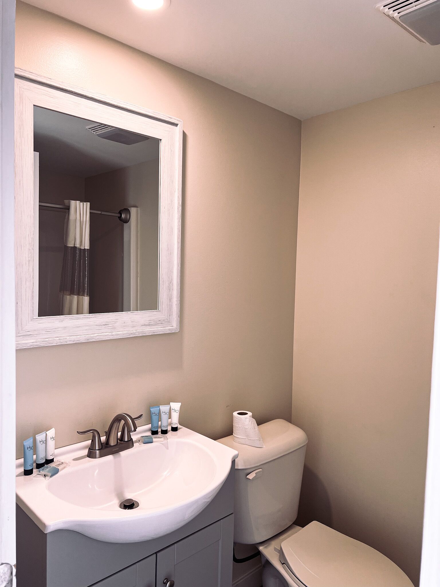 A bathroom with a white sink, mirror, and toilet. There are toiletries on the sink counter.