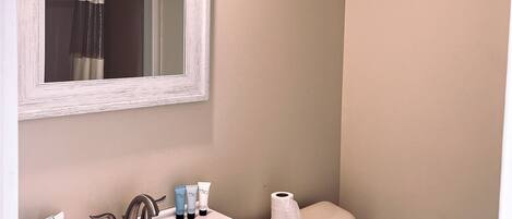 A bathroom with a white sink, mirror, and toilet. There are toiletries on the sink counter.