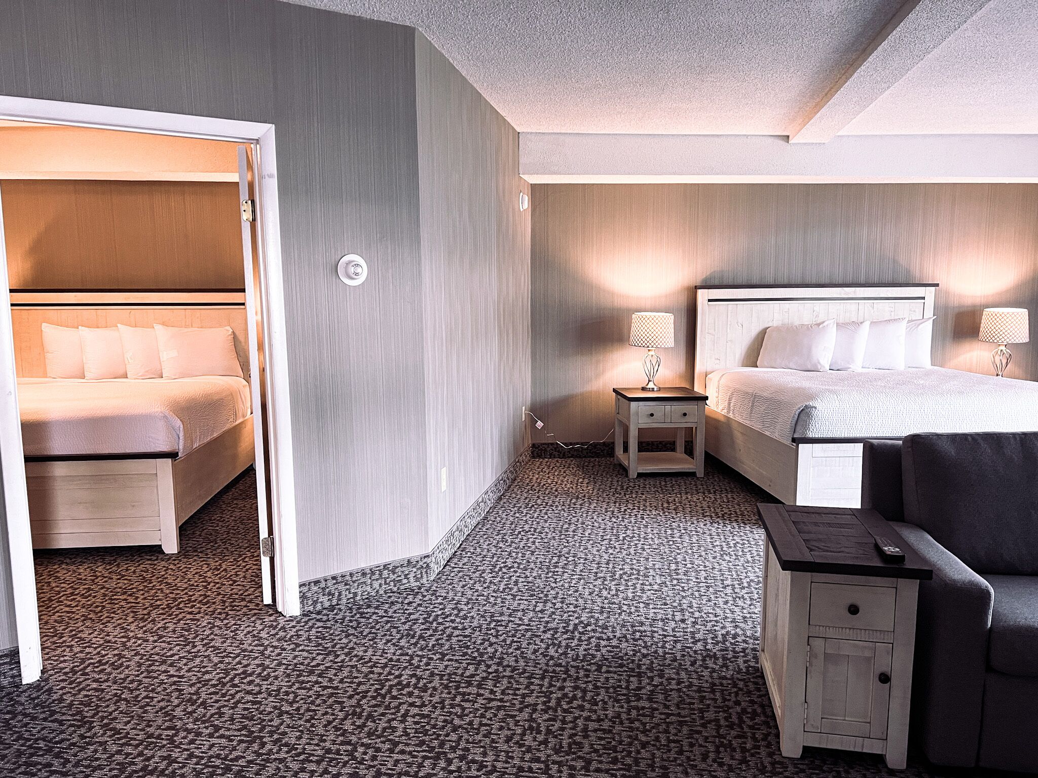 A hotel room with a bed, a chair, a nightstand, and a lamp.