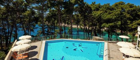 A swimming pool with lounge chairs and umbrellas, surrounded by trees and a view of the sea.