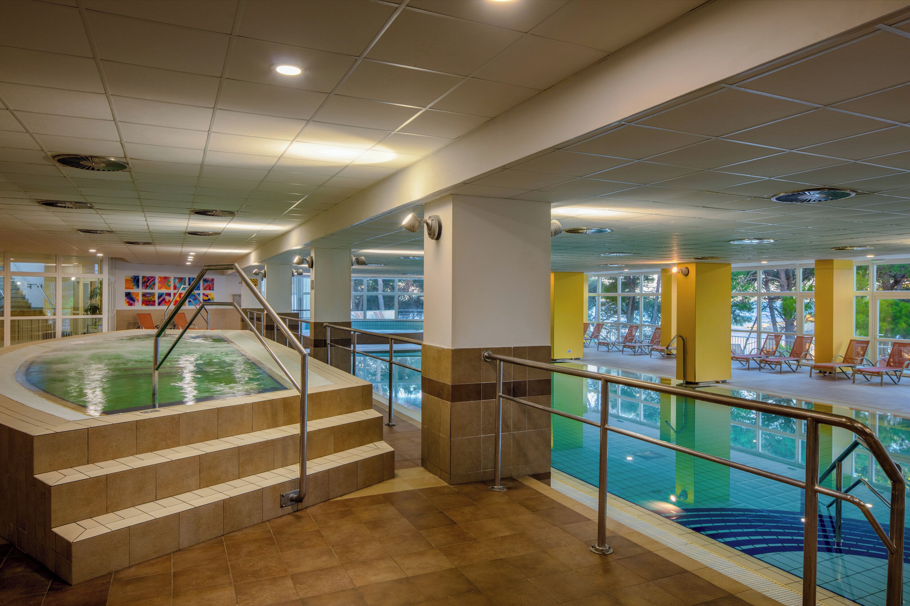 Un espace piscine avec des marches menant à l’eau, un toit ouvrant et un coin salon avec des chaises.