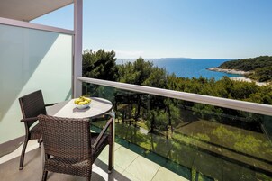 Un balcón con sillas de mimbre y una mesa, con vistas a un paisaje costero con árboles y el mar.