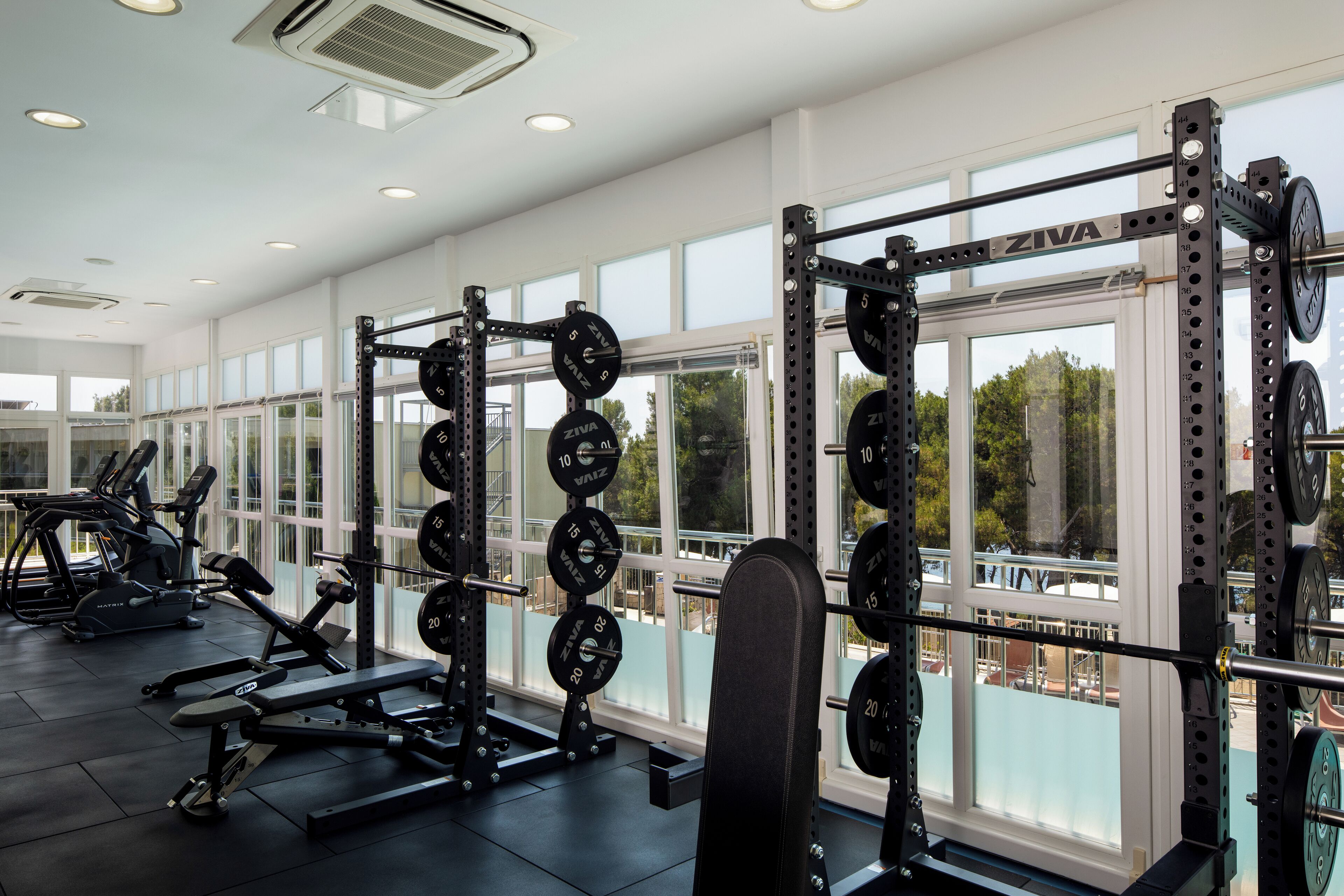 A gym with weightlifting equipment, large windows, and a view of the outside.