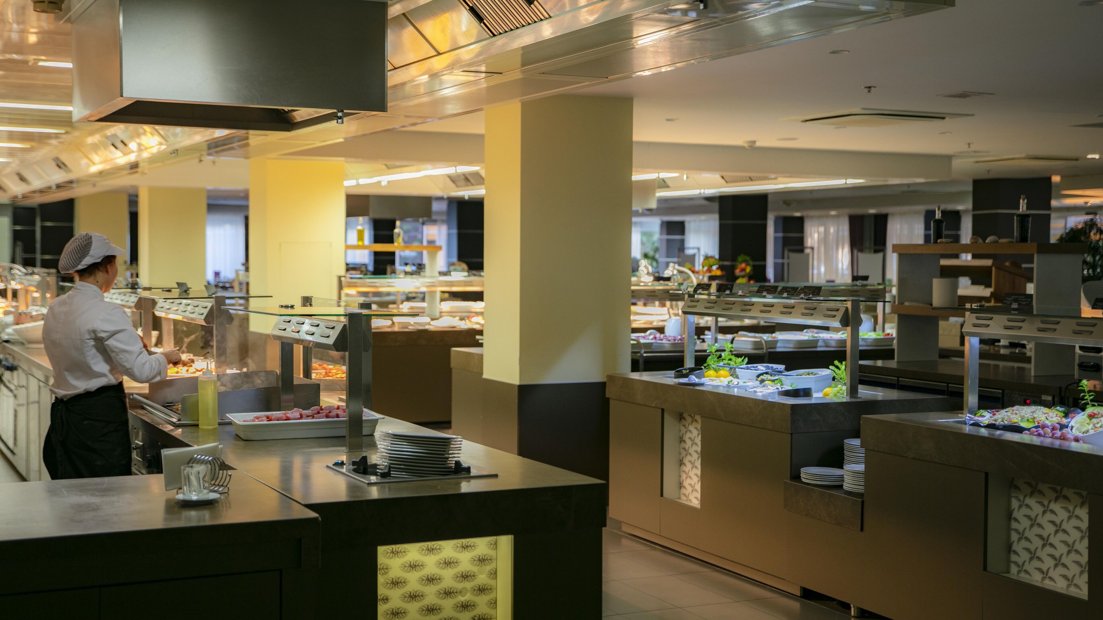 A buffet setup with various food stations and a staff member serving.