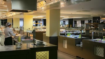 A buffet setup with various food stations and a staff member serving.