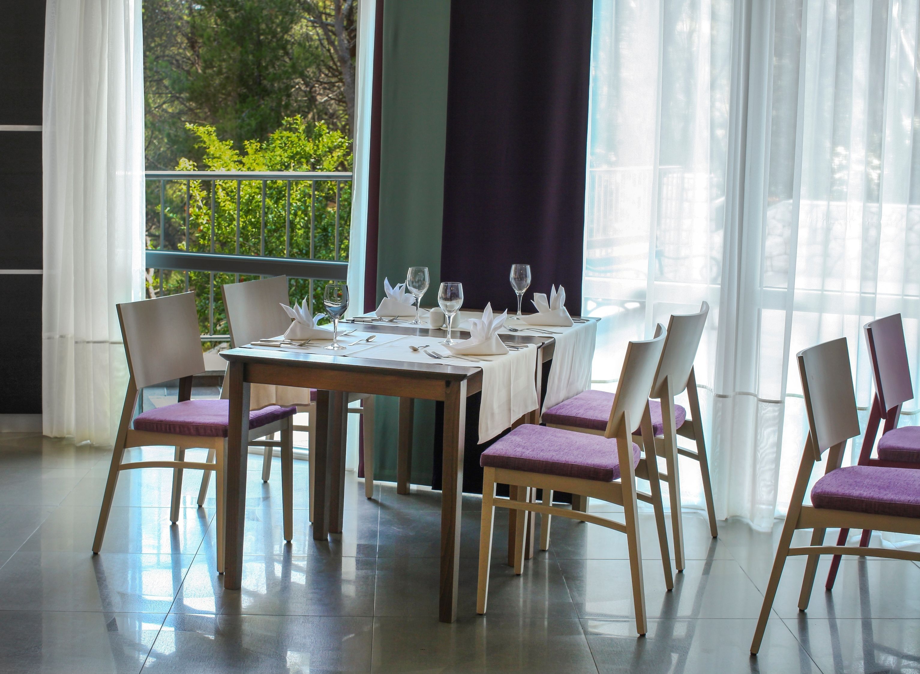 Un coin repas avec une table dressée pour six personnes, des chaises avec des coussins et une vue sur la verdure environnante.