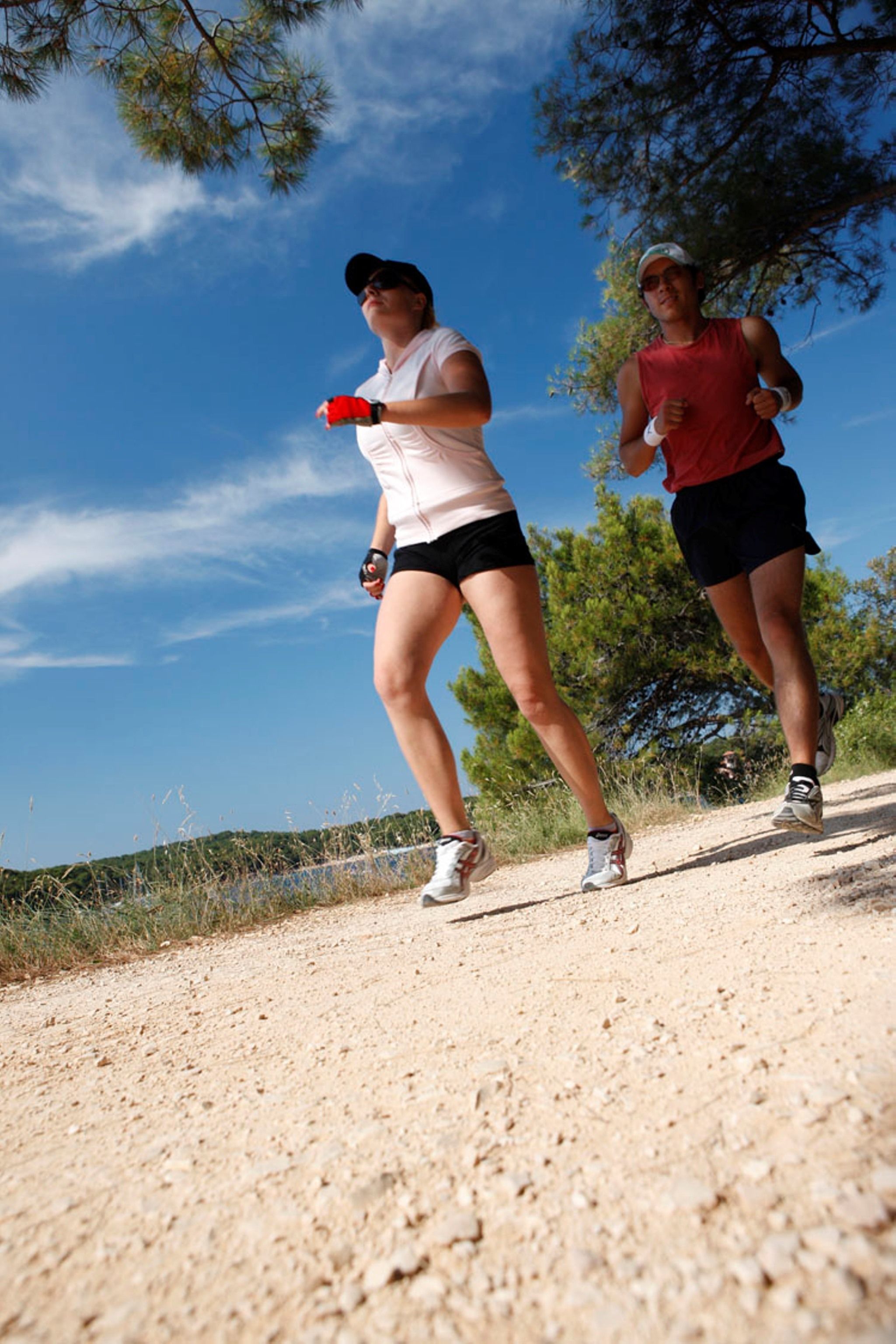 Dos personas trotando por un sendero de tierra con árboles y un cielo despejado al fondo.