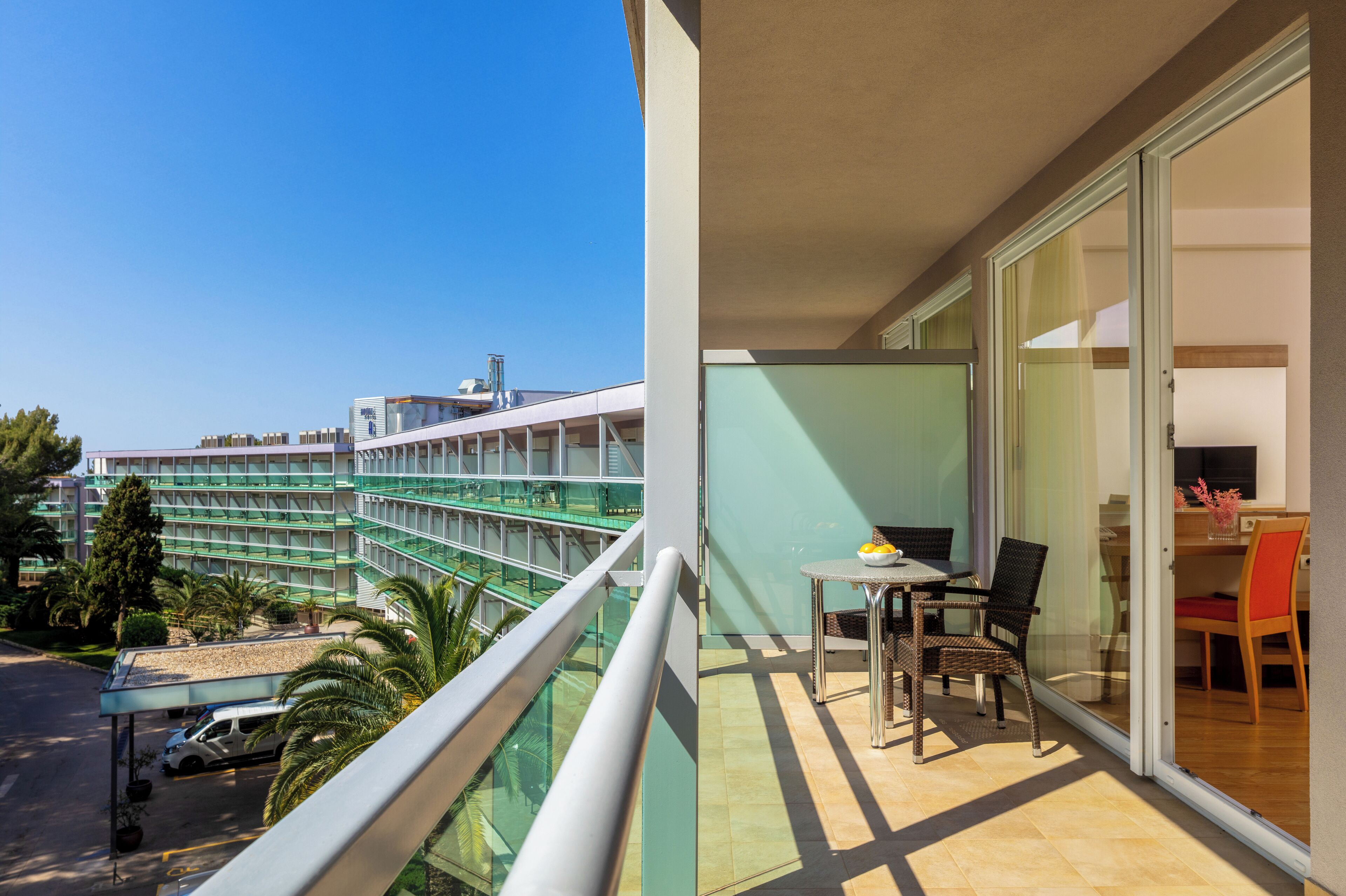 A balcony with a table and chairs, a glass door, and a view of a hotel building.