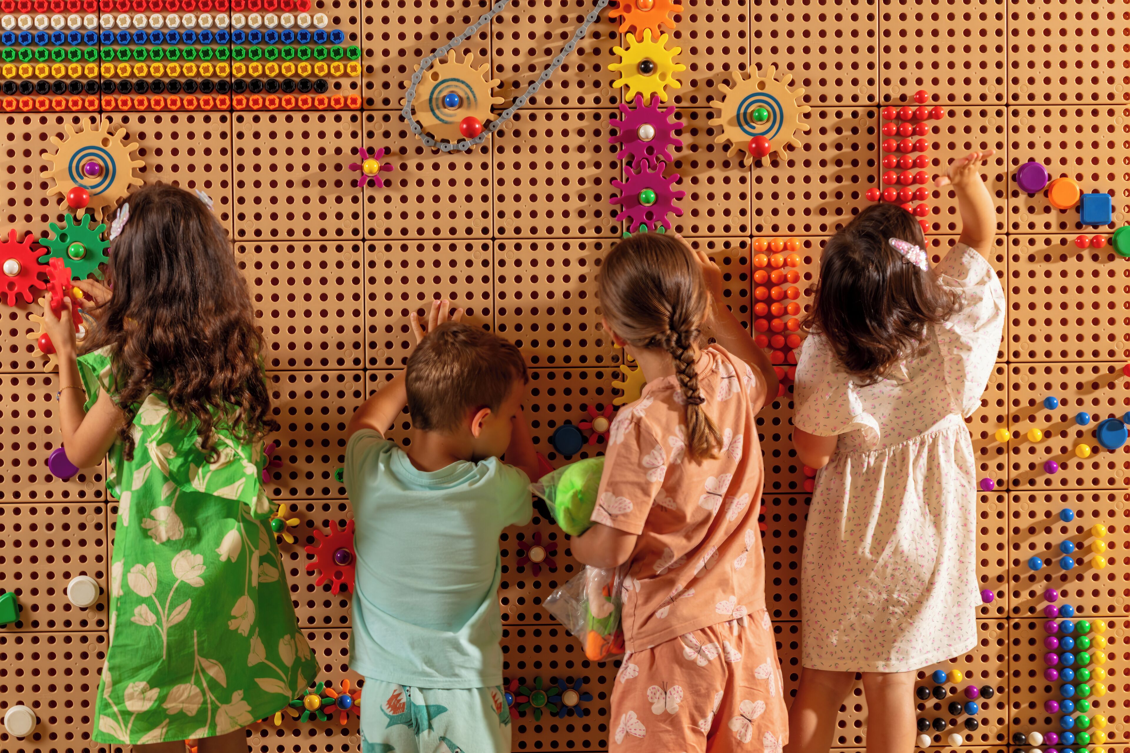 Children playing with toys on a pegboard wall.