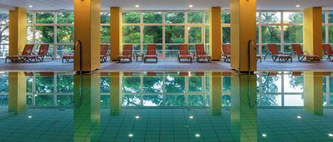 A large indoor swimming pool with multiple sun loungers and large windows.