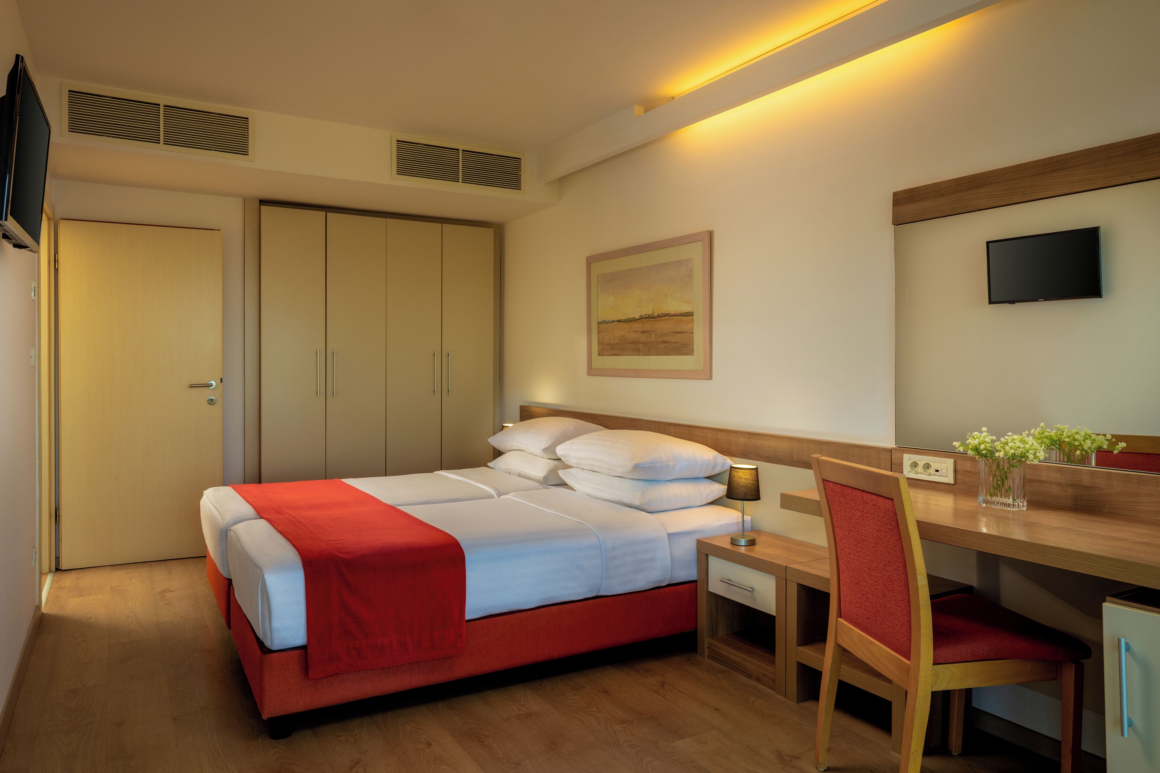 Ein Hotelzimmer mit Bett, Schreibtisch, Stuhl, Fernseher und einem Bild an der Wand.