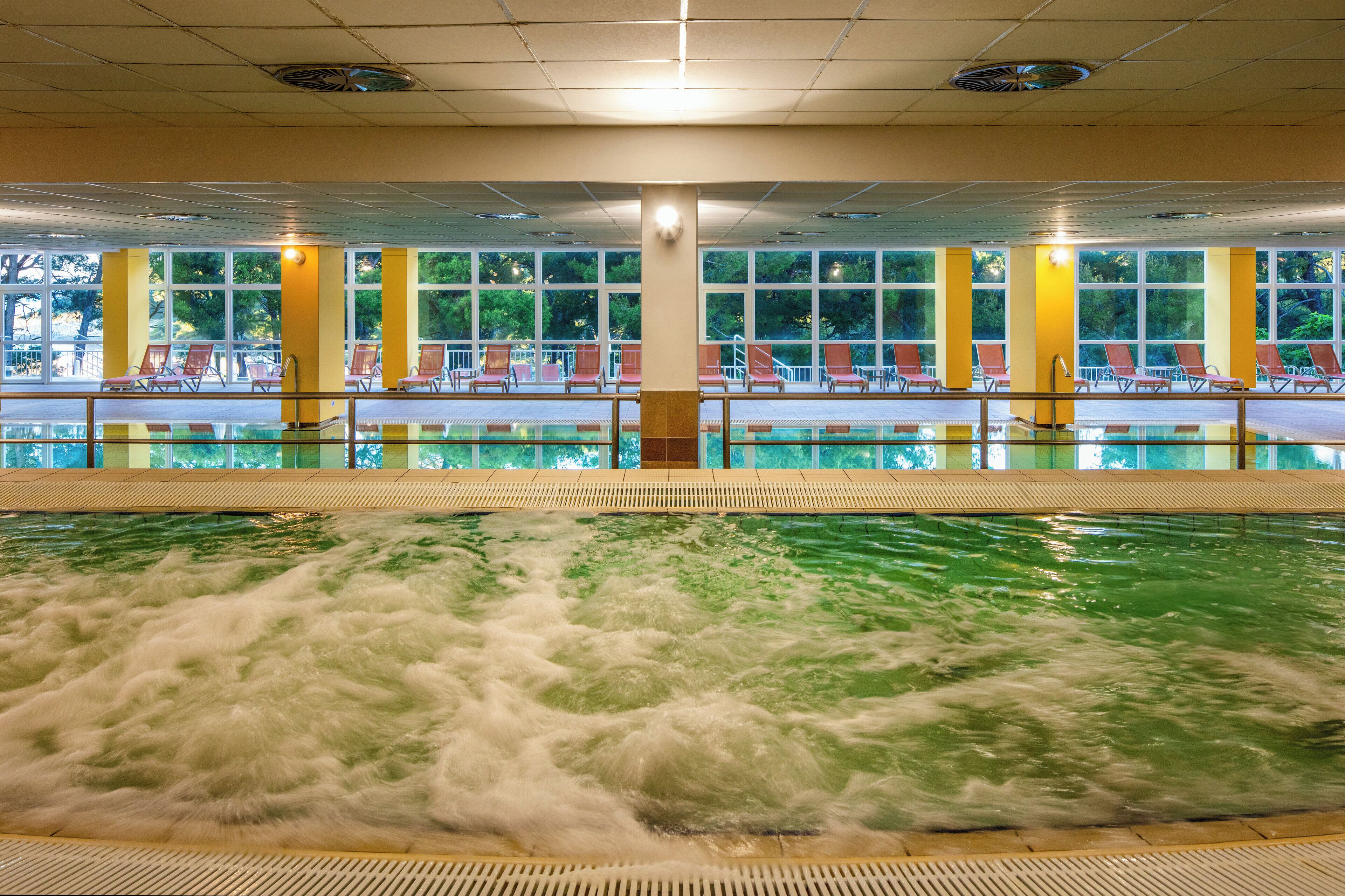 An indoor swimming pool with multiple lanes, surrounded by sun loungers and large windows.