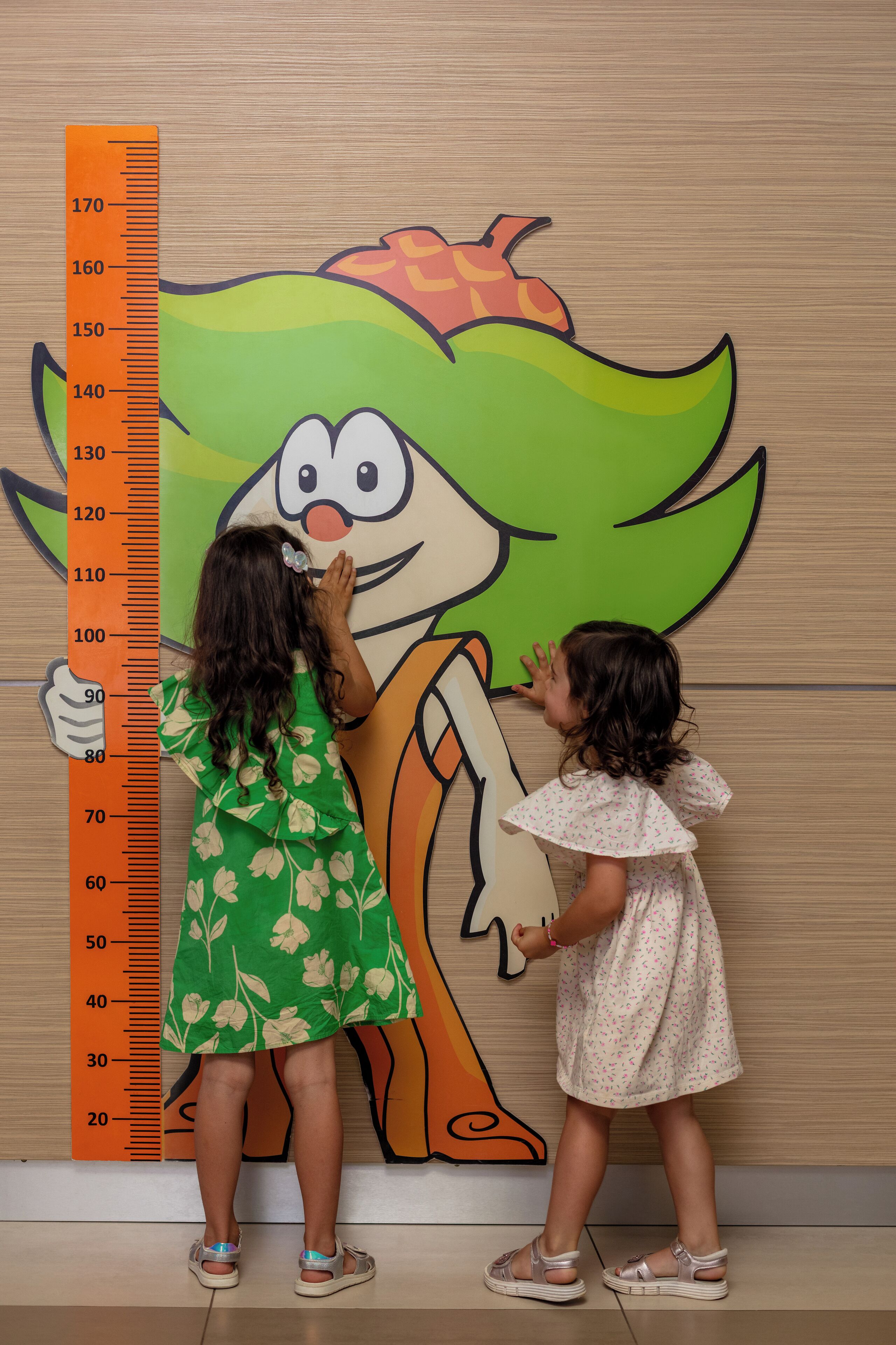 Two children measuring a cartoon character with a height chart.