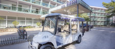 A golf cart parked in front of a hotel with a glass facade and multiple balconies.