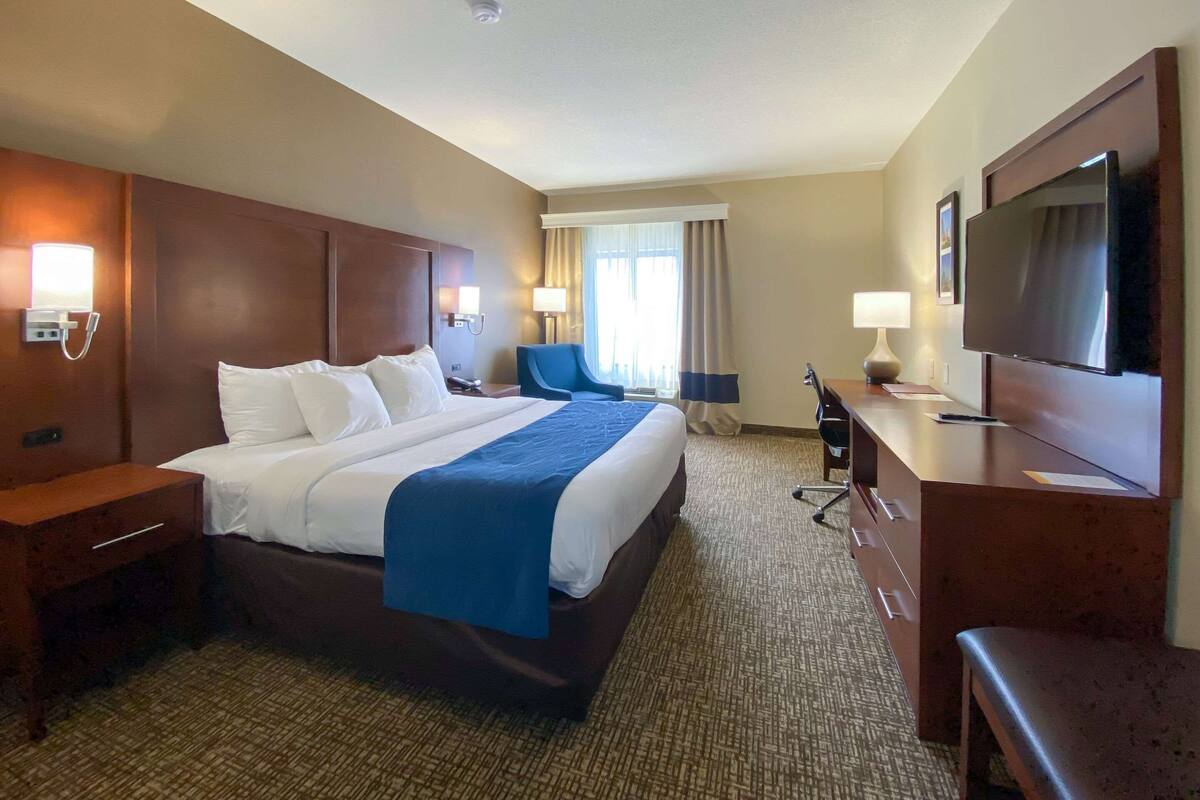 Habitación de hotel con una cama grande, un escritorio, una silla, un televisor y una ventana con cortinas.