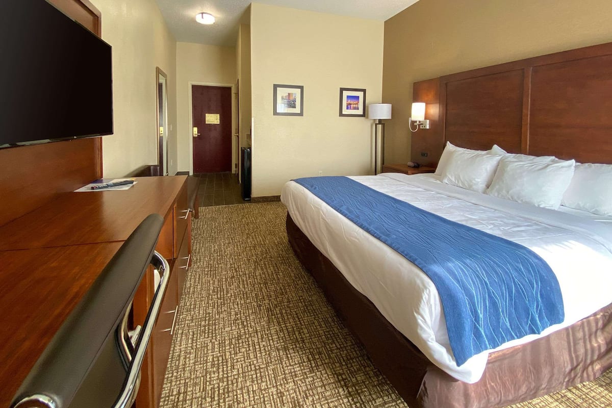 Una habitación de hotel con una cama grande, un escritorio, un televisor de pantalla plana, una lámpara y una puerta que da a otra habitación.