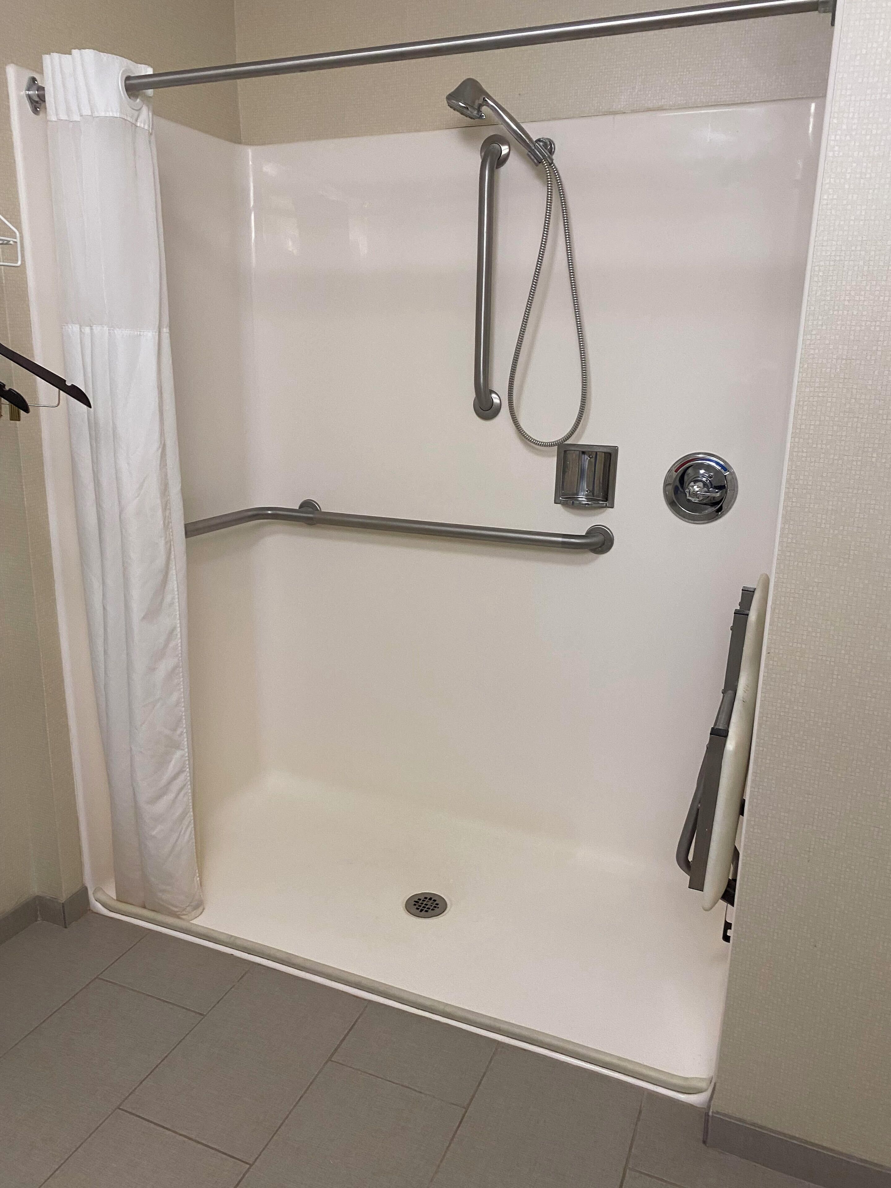 A walk-in shower with a grab bar, a showerhead, and a handheld shower attachment.