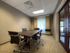 A conference room with a long table, four chairs, a ceiling light, and a door with a view outside.