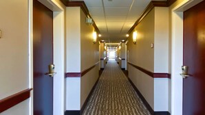 A long, narrow hotel corridor with carpeted floors, wooden trim, and wall-mounted lights. - Comfort Inn East Windsor - Springfield (East Windsor)