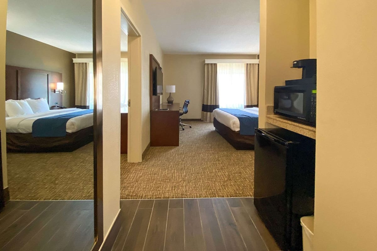 Habitación de hotel con dos camas, un escritorio, una silla, un televisor y un microondas.
