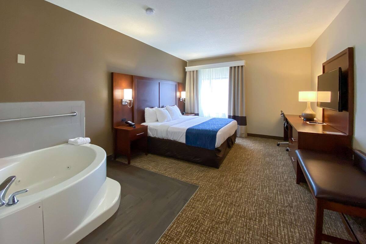 Habitación de hotel con una cama grande, baño independiente con bañera, escritorio con silla y televisor.