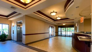 A spacious hotel lobby with a wooden herringbone floor, a reception desk, and a large glass door leading outside. - Comfort Inn East Windsor - Springfield (East Windsor)