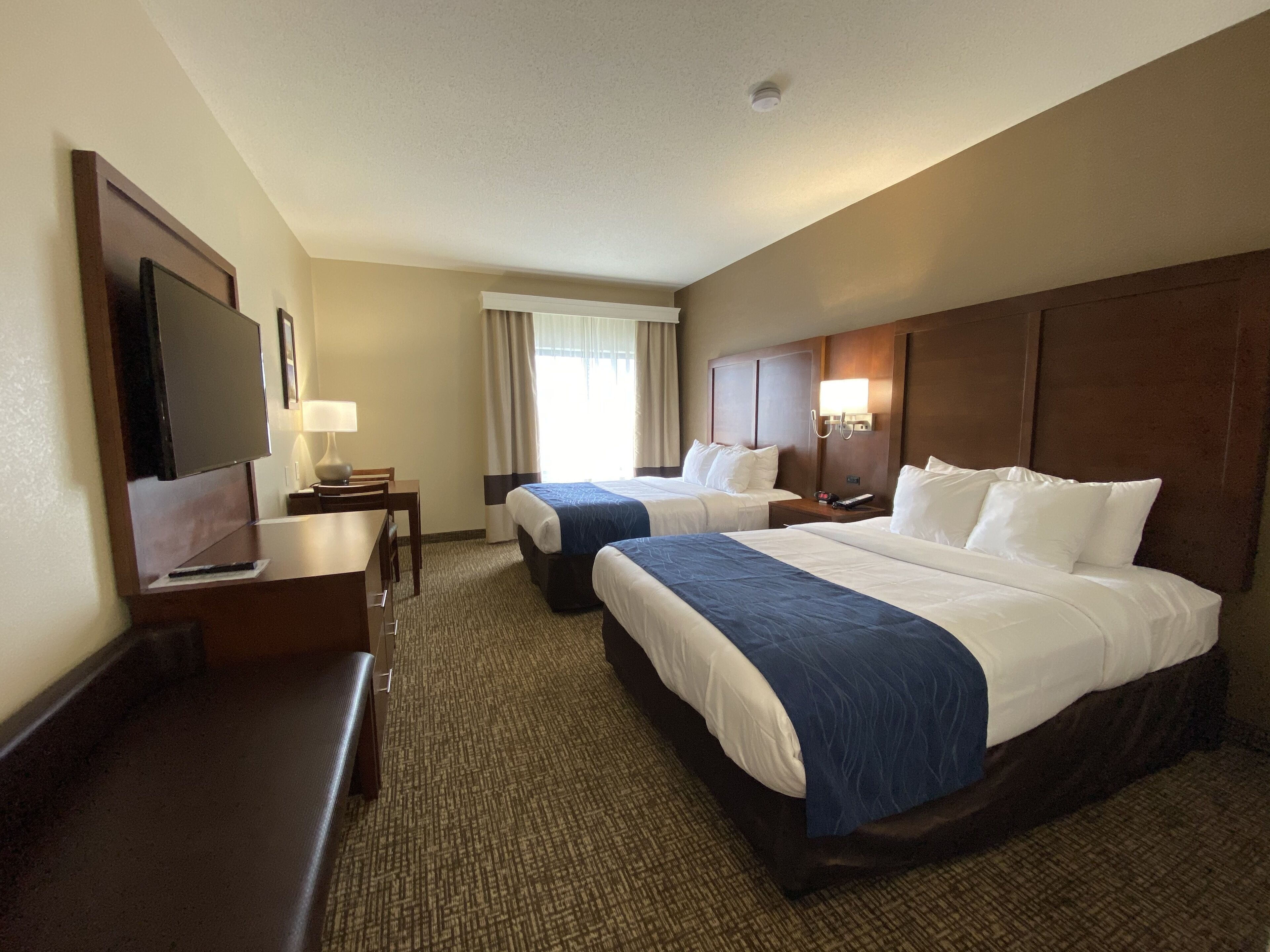 A hotel room with two beds, a desk, a TV, and a window with curtains.
