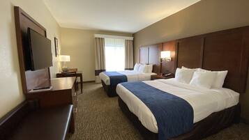 A hotel room with two beds, a desk, a TV, and a window with curtains.