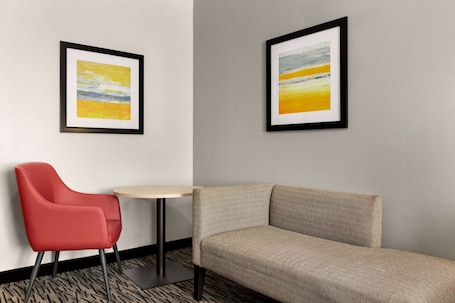 A modern hotel room with a red chair, a beige sofa, and two framed abstract paintings on the wall.