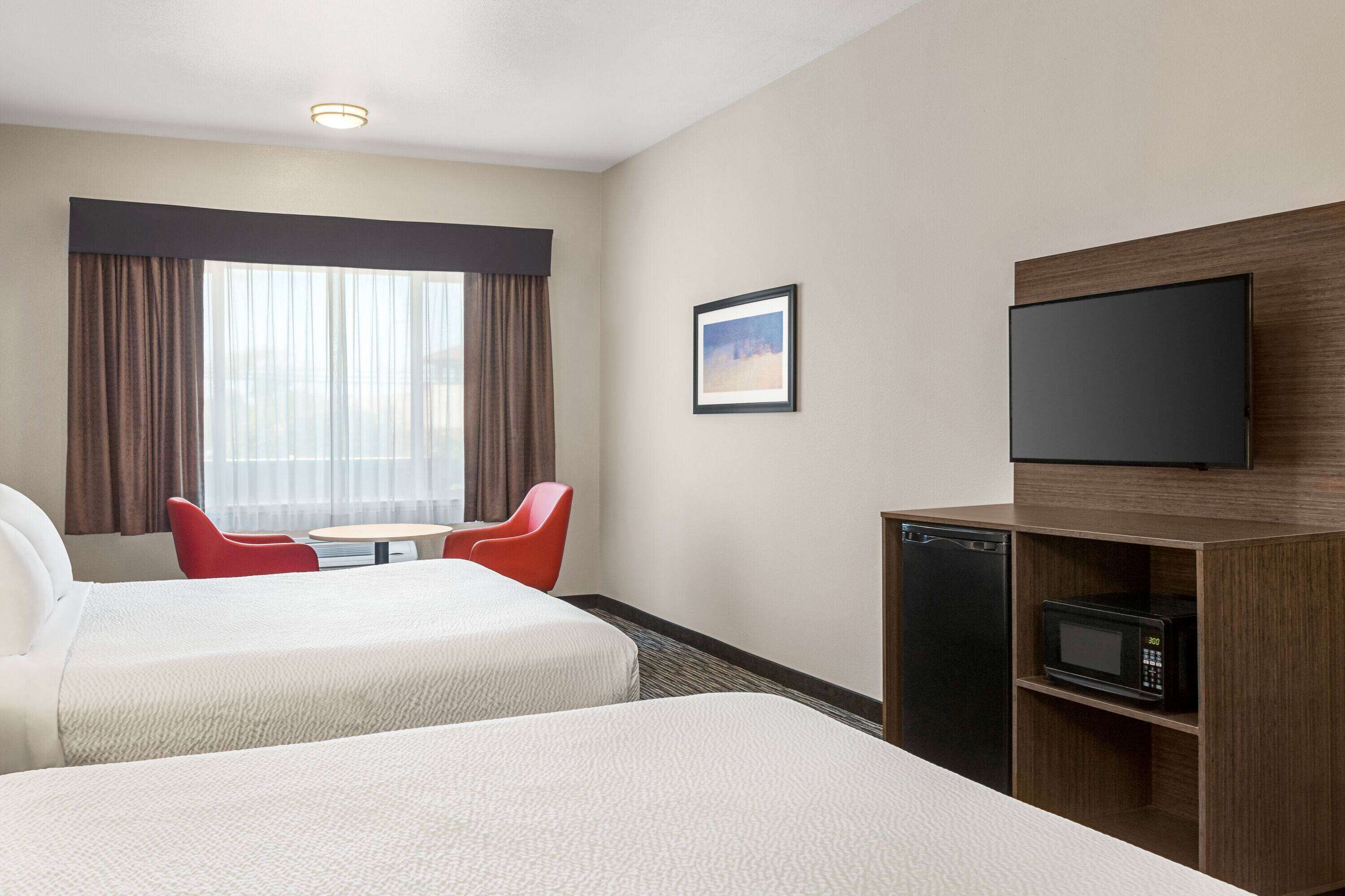 Habitación de hotel con dos camas, televisión, microondas, una mesita y una silla roja.