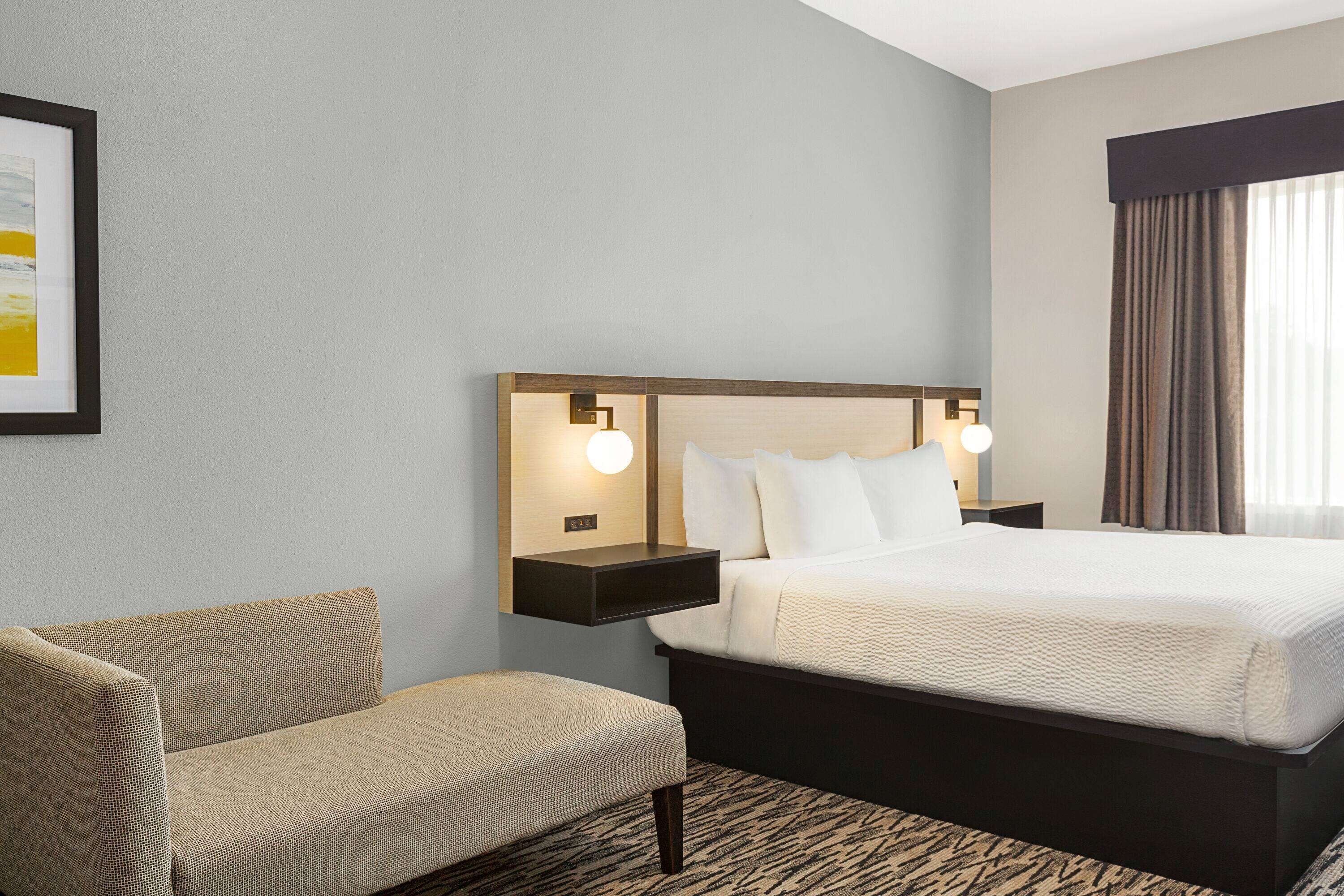Une chambre d’hôtel comprenant un lit, une table de chevet, une chaise et un luminaire fixé au mur.
