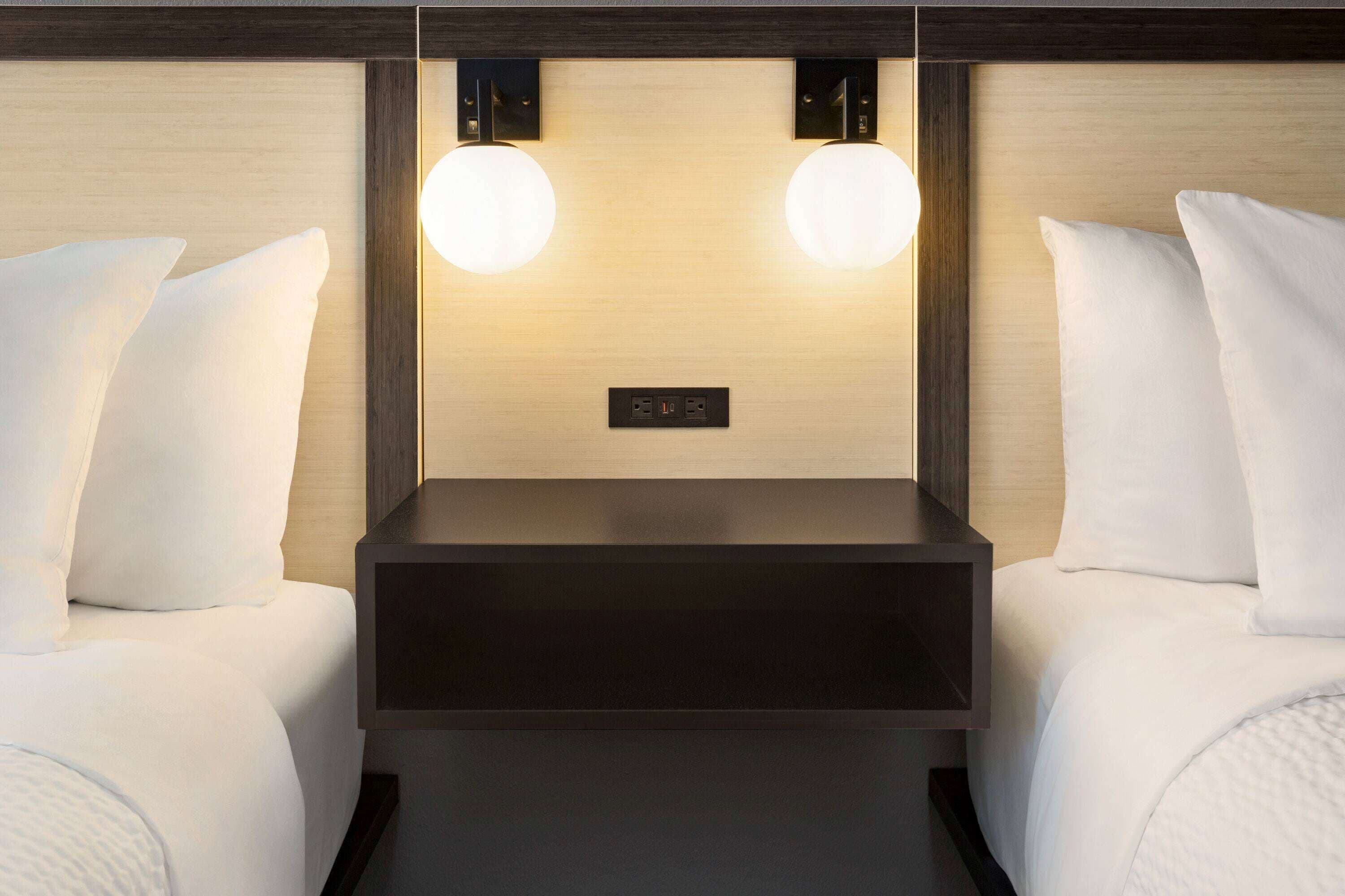 Ein Hotelzimmer mit zwei Betten, einem Holz-Kopfteil, einem Nachttisch und zwei Wandleuchten.