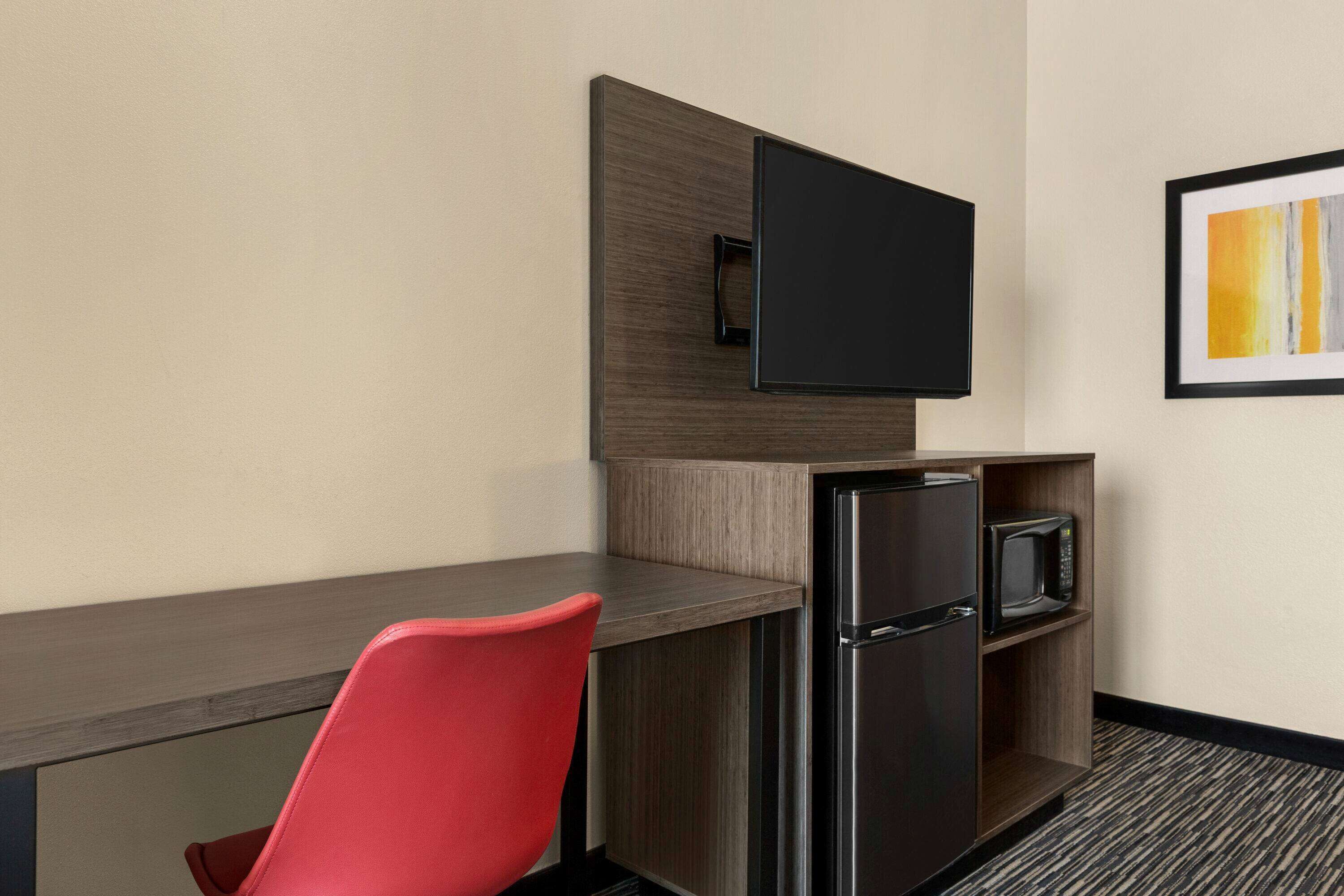 Quarto de hotel compacto com cozinha compacta, televisão de tela plana na parede, micro-ondas e geladeira.