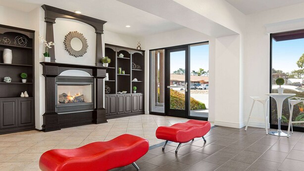 A modern living room with a fireplace, red chairs, and a view through large glass doors. - Ramada by Wyndham Marina (Marina)